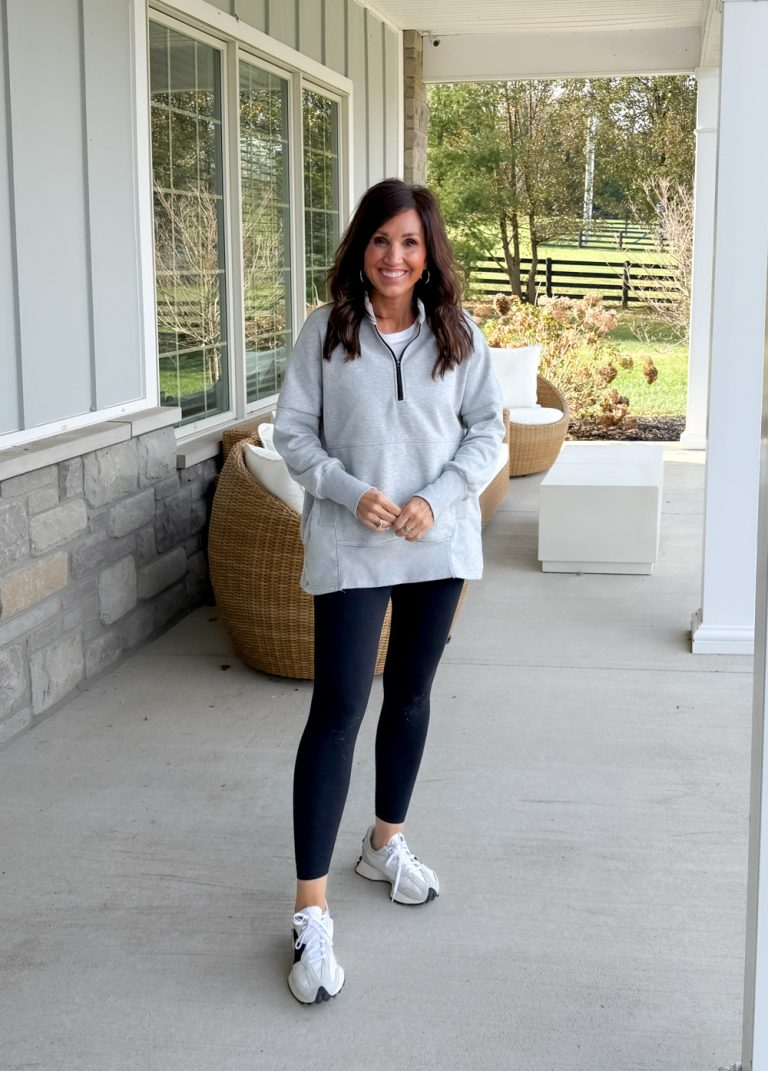Cyndi wearing a light gray half zip pullover with black leggings and white sneakers, a casual fall athleisure outfit perfect for errands or relaxing at home.