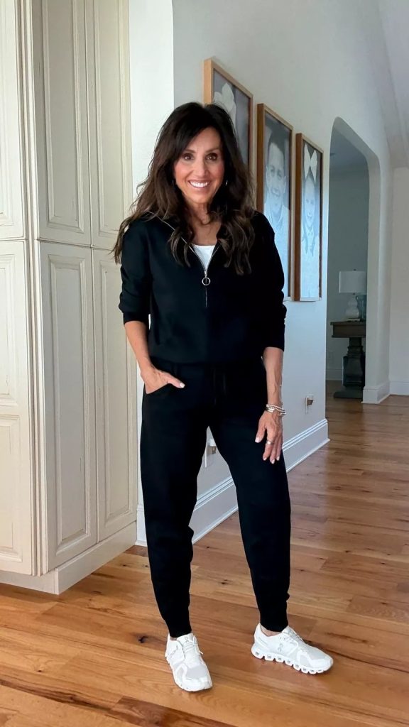 Cyndi in a black half zip tracksuit with jogger pants, styled with a white tank underneath and white sneakers for a casual fall look.