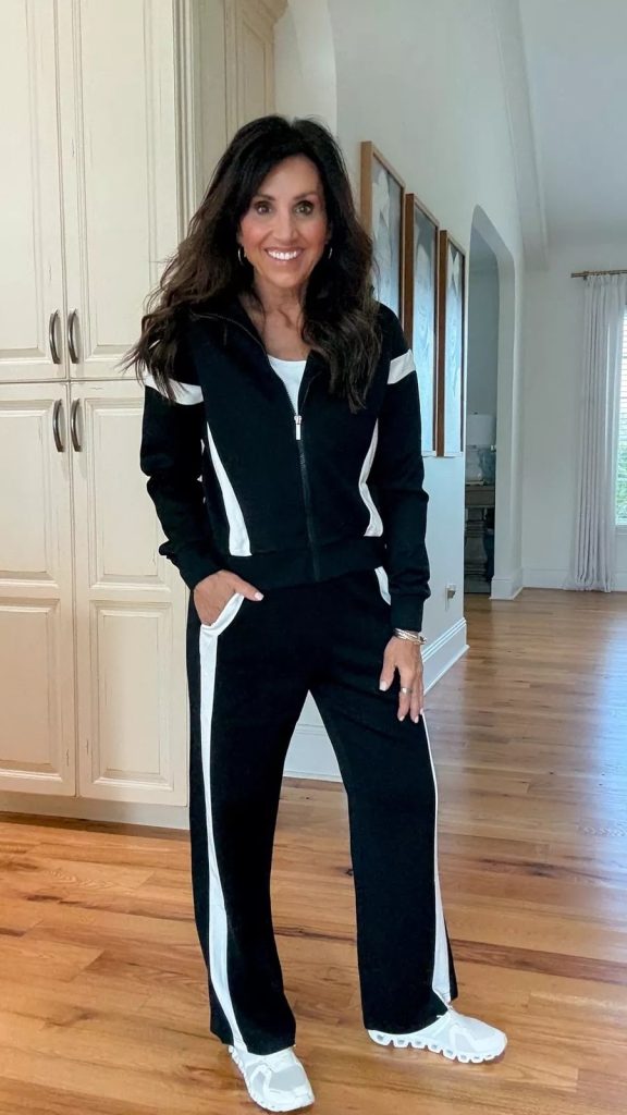 Cyndi wearing a black and white colorblock zip up jacket with matching wide leg pants and white sneakers, an athleisure set perfect for fall.