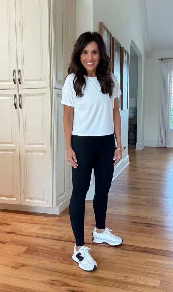 Cyndi wearing a white short sleeve tee with black leggings and white sneakers, a simple fall athleisure outfit for everyday wear.