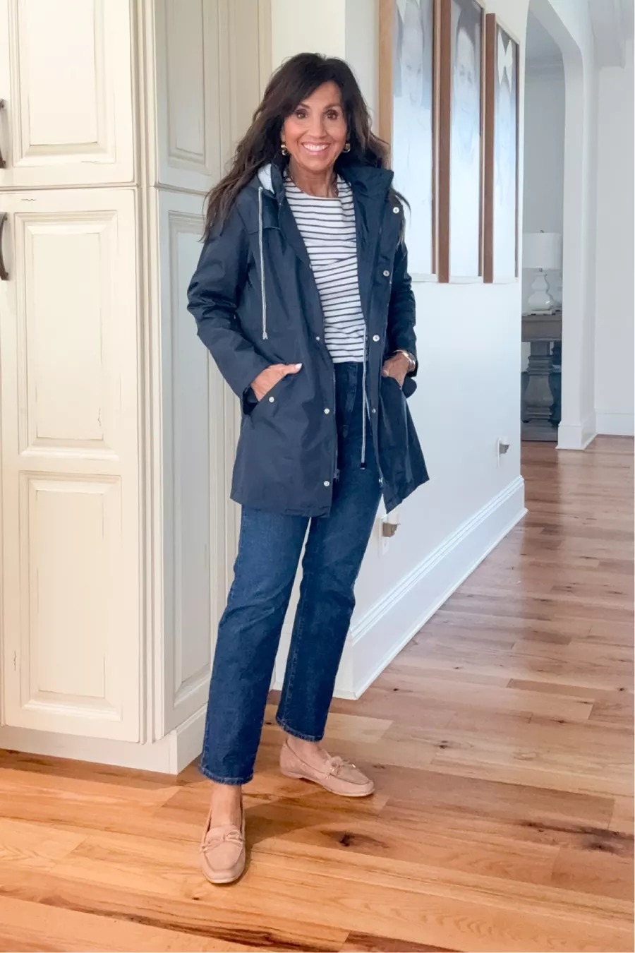 Cyndi styled in a navy hooded rain jacket with a striped tee, straight-leg jeans, and loafers, a practical fall outfit for rainy days.