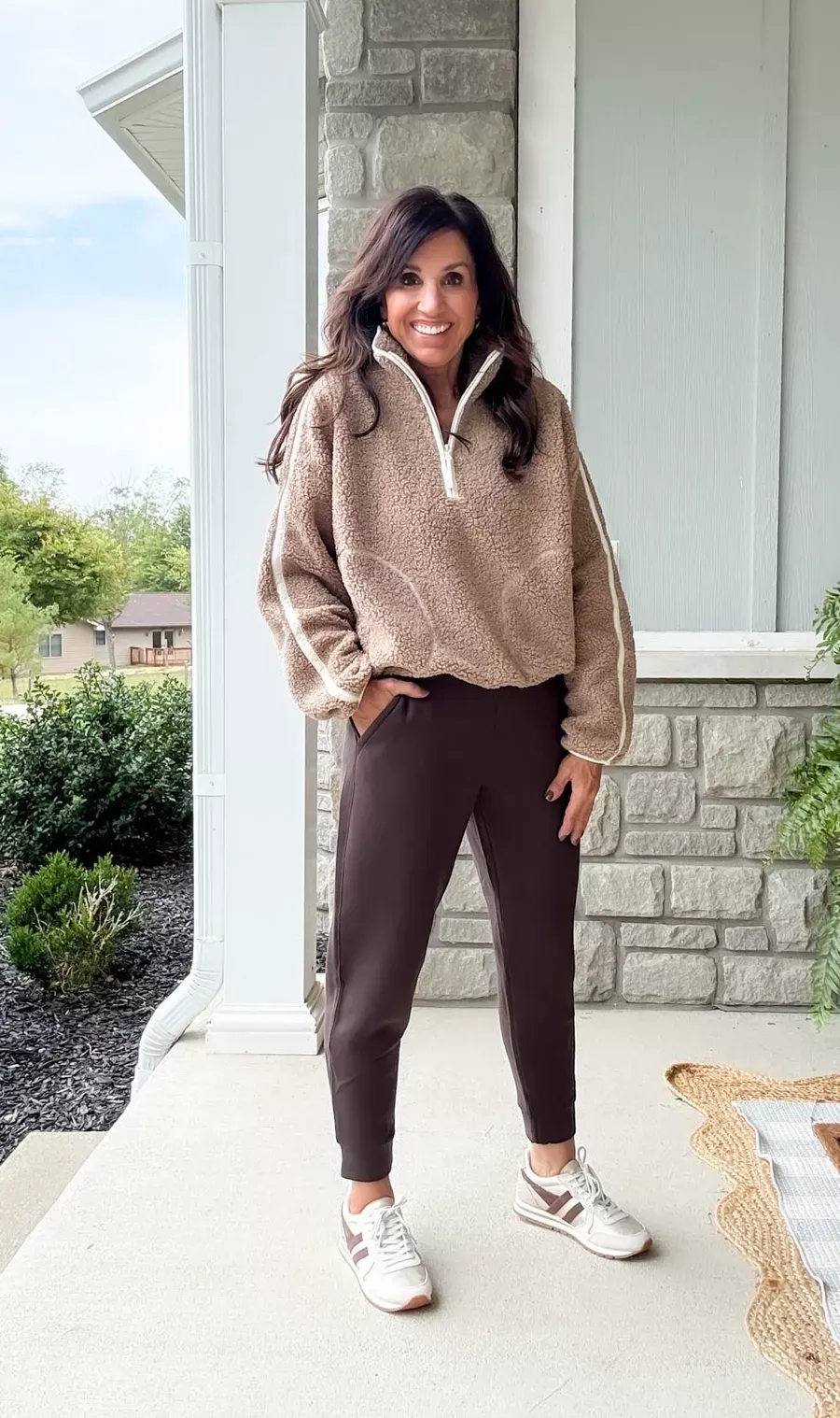 Woman wearing a tan sherpa half-zip pullover with brown joggers and white sneakers, a cozy and casual Thanksgiving weekend outfit for women over 50.