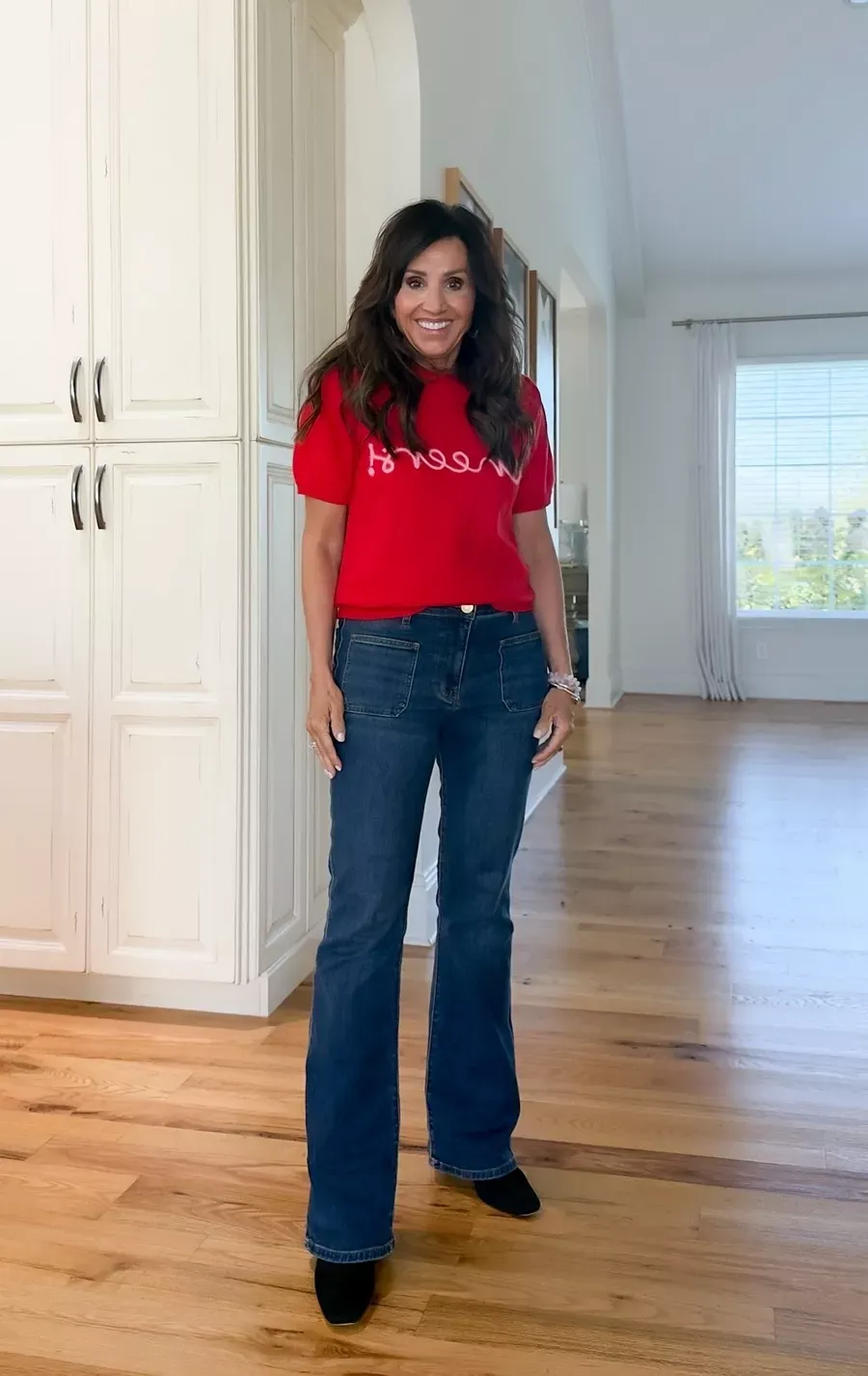 Cyndi Spivey wearing a red sweater tee with dark flare jeans and black booties, a casual and festive outfit for the holidays.