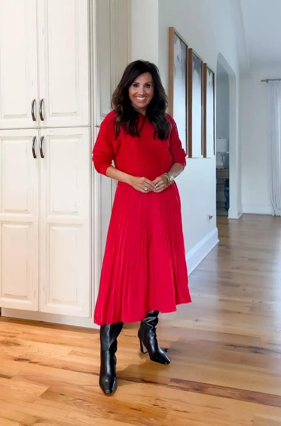 Cyndi Spivey wearing a red pleated midi skirt with a matching red sweater and black knee-high boots, a classic monochromatic holiday outfit.