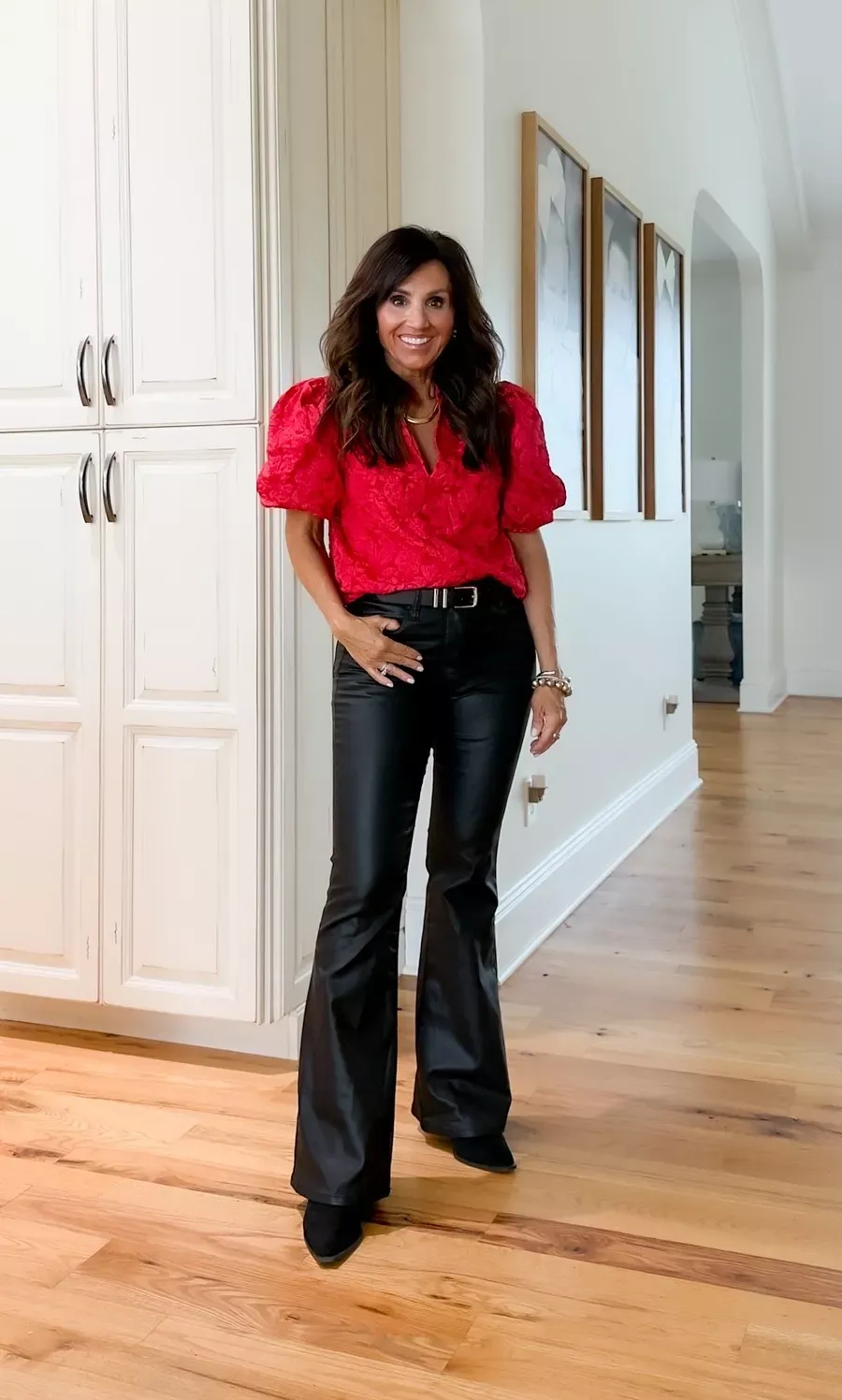 Cyndi Spivey wearing a red puff-sleeve blouse with coated black jeans and heels, a festive and flattering holiday outfit.
