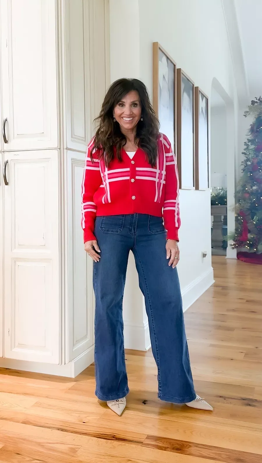 Cyndi Spivey wearing a red plaid cardigan with wide-leg blue jeans and neutral pointed-toe flats in a holiday-decorated home.