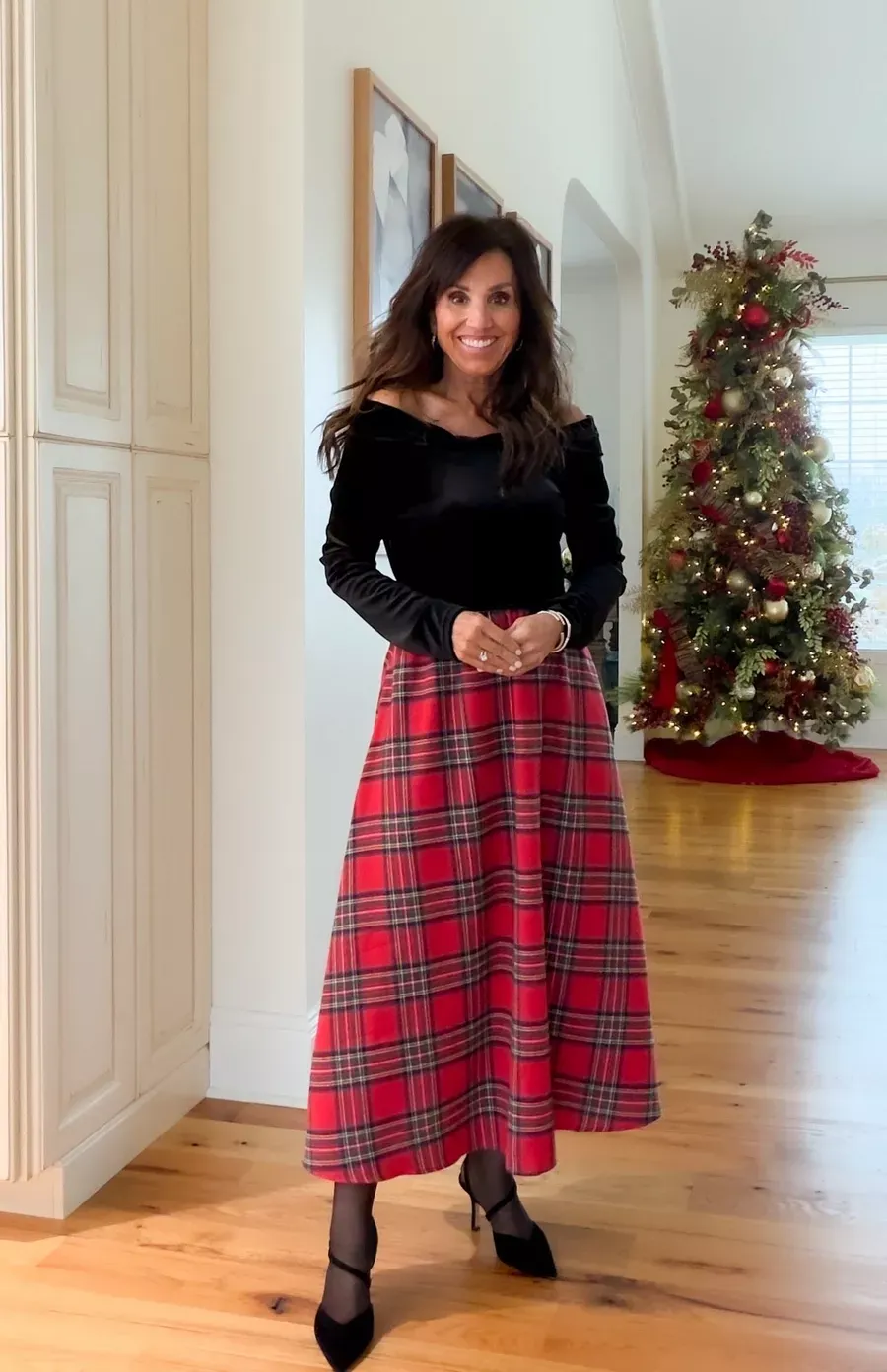 Cyndi Spivey wearing a dress with an off-the-shoulder black top and long red plaid Christmas skirt and black heels.