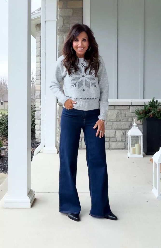 Cyndi Spivey wearing a gray patterned sweater with dark wash wide-leg jeans and black ankle boots, styled for a casual winter outfit on a front porch.