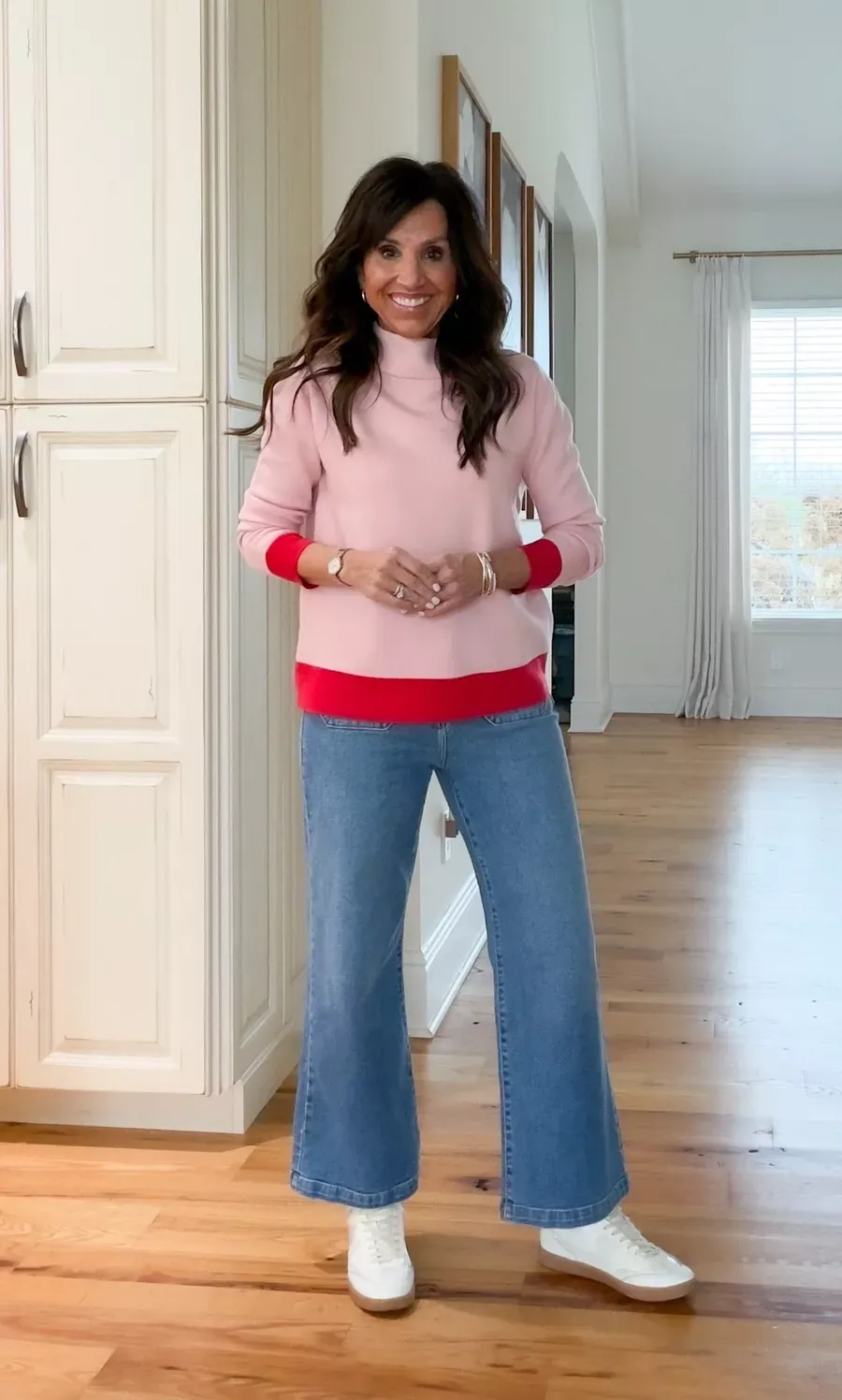Cyndi Spivey wearing a colorful winter outfit made of a pink and red colorblock sweater with light wash wide-leg jeans and white sneakers